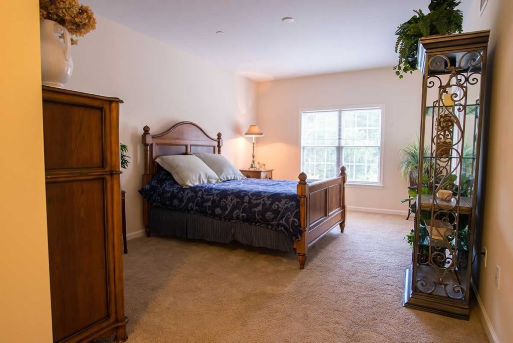 A cozy bedroom with a wooden bed, bedside lamp, and large window.