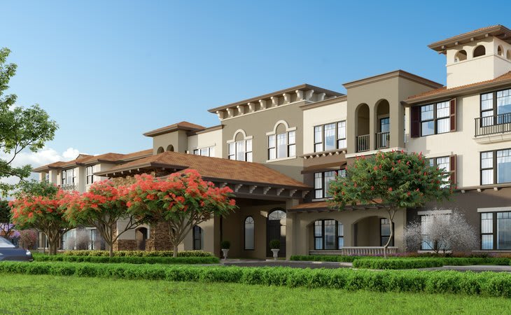 A Mediterranean-style building with lush landscaping and a clear blue sky.