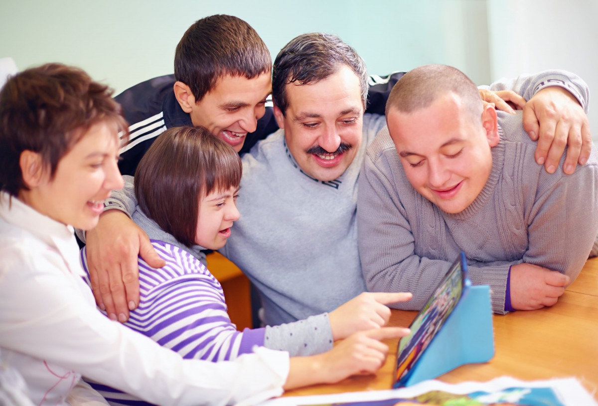A diverse group of people smiling and gathered around a tablet.