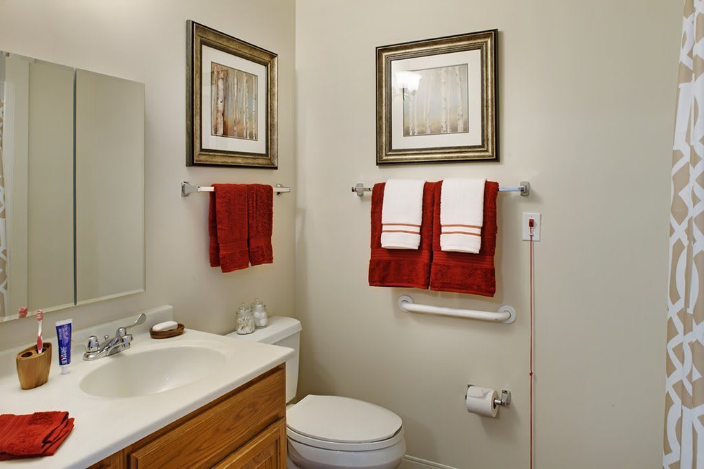 A neatly organized bathroom with red and white towels, framed artwork, and a clean sink area.