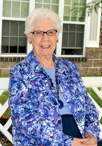 A cheerful elderly woman in a vibrant blue floral jacket, enjoying a sunny day outdoors.