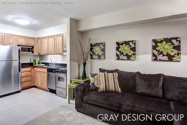 A modern living area with a connected kitchen, featuring a dark sofa and floral artwork on the wall.