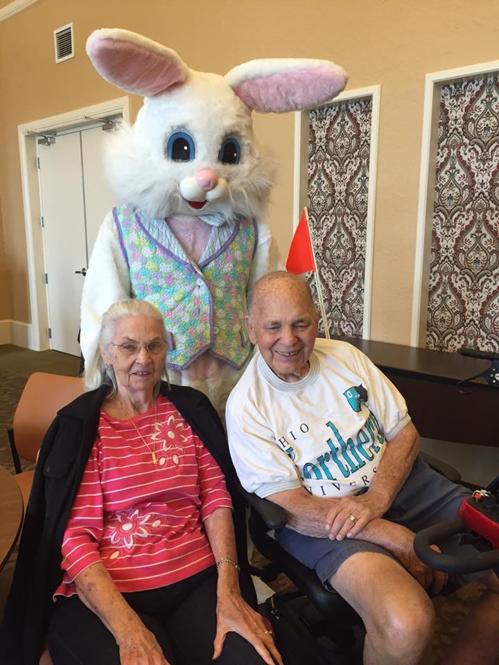 An elderly couple sitting with the Easter Bunny, enjoying a festive occasion indoors.