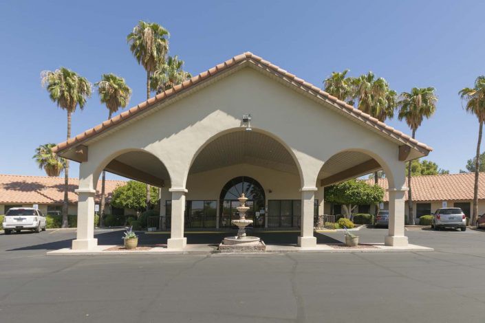 An elegant building entrance with arches and a central fountain, surrounded by palm trees.