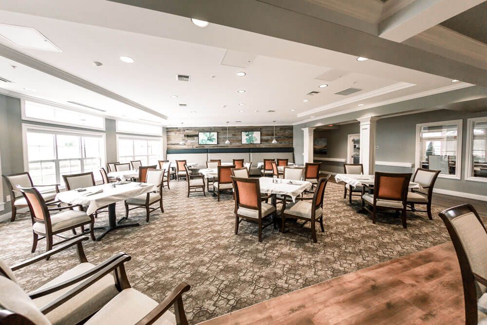 An empty dining area with neatly arranged tables and chairs, featuring large windows and elegant decor.