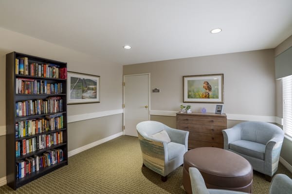 A cozy office space featuring a bookshelf, comfortable chairs, and wall art.