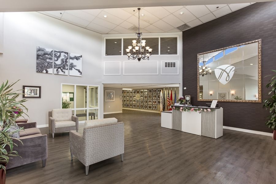 A modern lobby with elegant furniture and a chandelier, featuring artwork and a reception area.