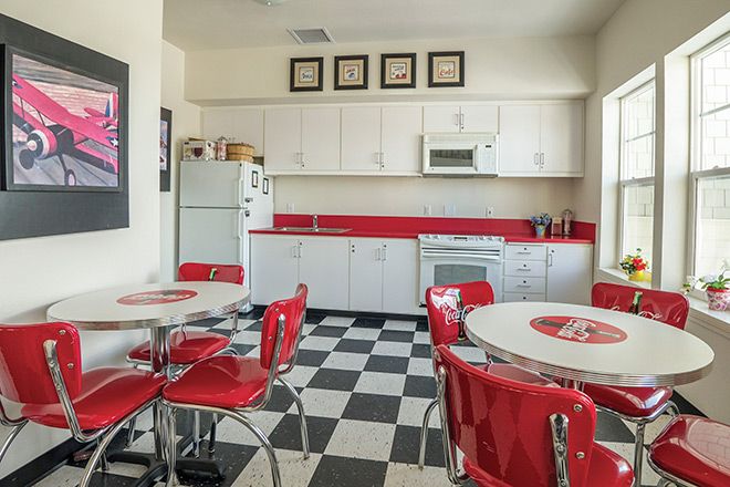 A retro-style kitchen with red accents and a black-and-white checkered floor, featuring diner-style seating.