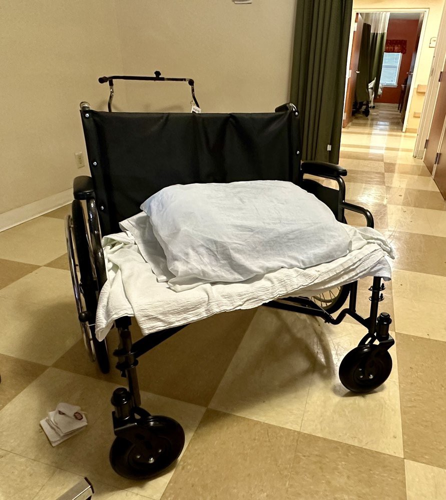 A wheelchair with a blanket draped over it, situated in a hallway.