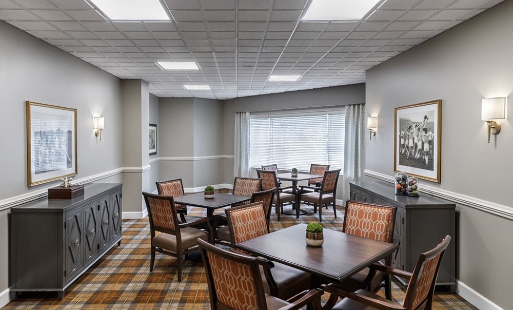 A cozy dining area with multiple tables and chairs, featuring large windows and ceiling lighting.