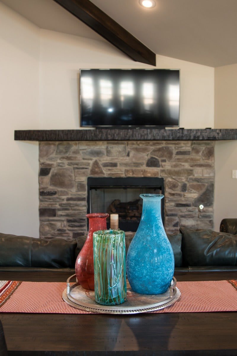 A cozy living room with a stone fireplace, mounted TV, and colorful vases on the table.