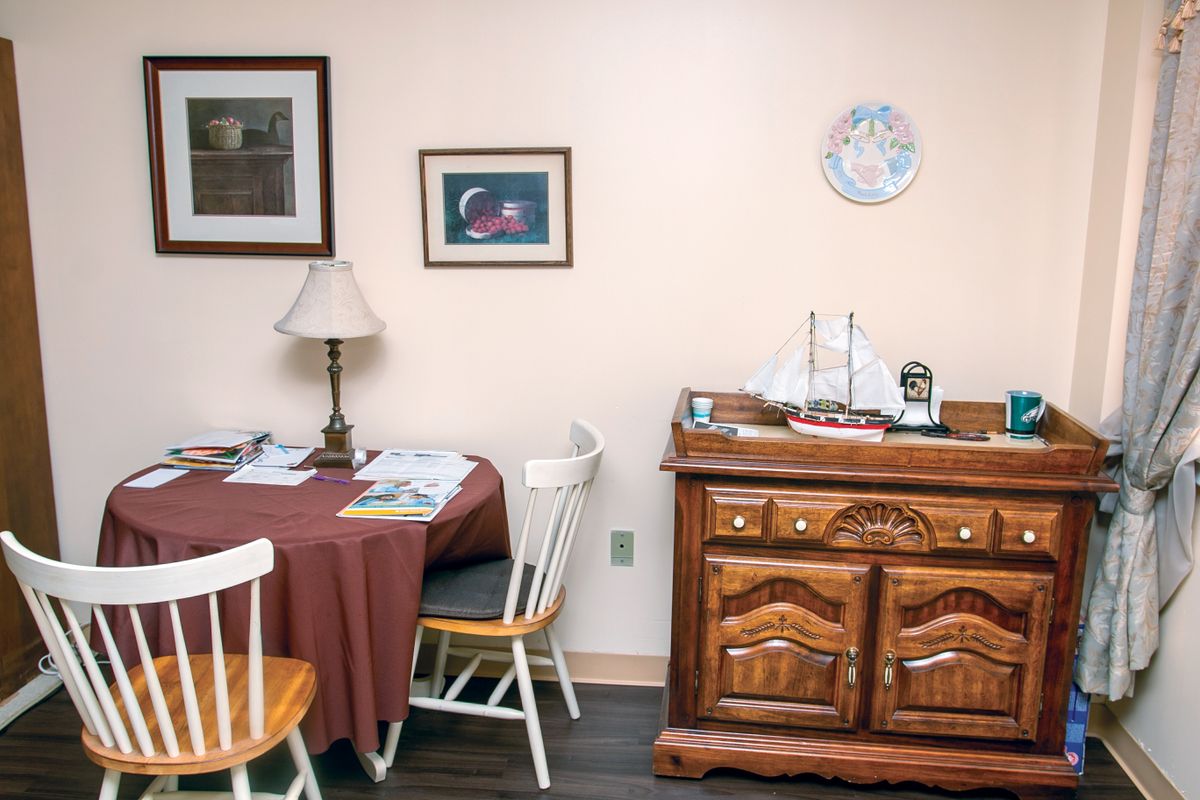 A cozy dining area with a round table, chairs, lamp, and decorative cabinet.