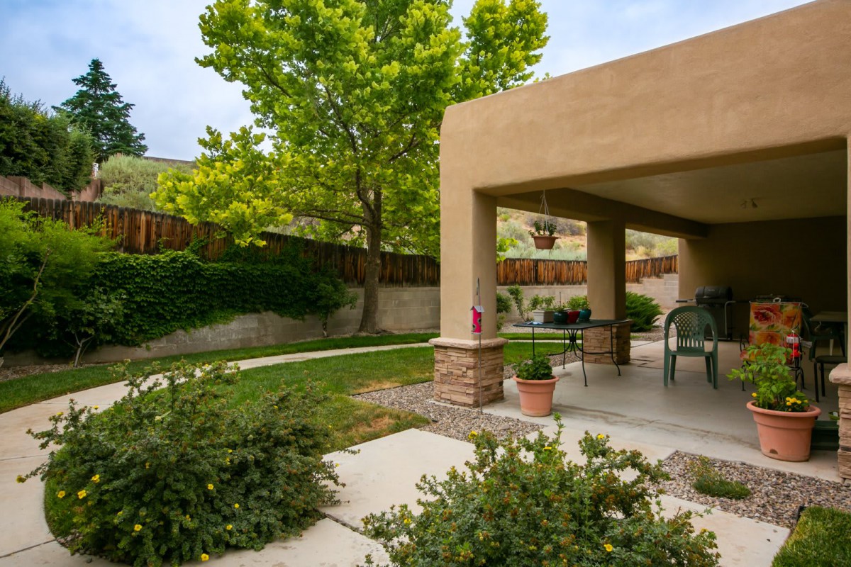 A peaceful backyard garden with a shaded patio and outdoor seating, surrounded by lush greenery.