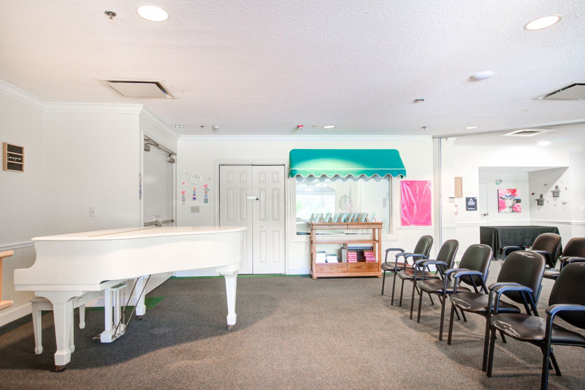 A bright waiting area featuring a white piano and a row of chairs.