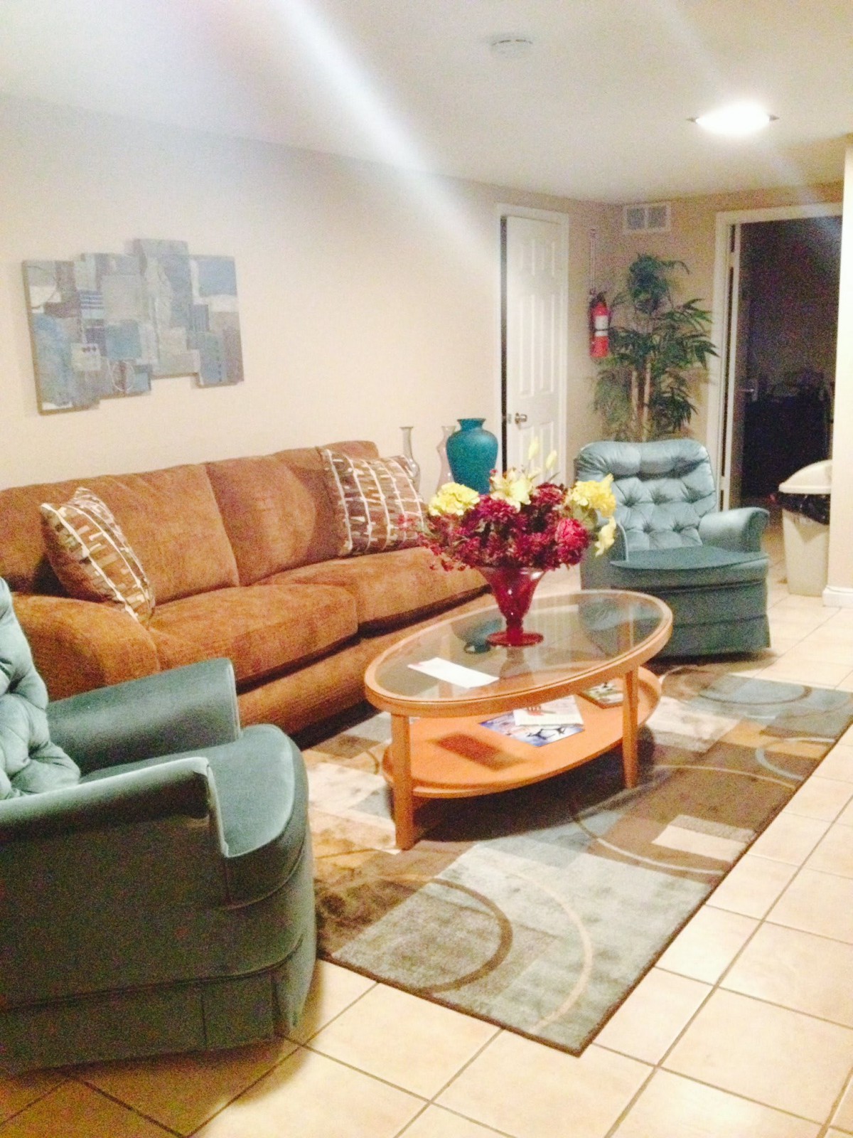 A cozy living room with a brown sofa, two blue armchairs, and a glass coffee table decorated with flowers.