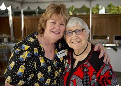 Two women smiling and embracing each other outdoors.