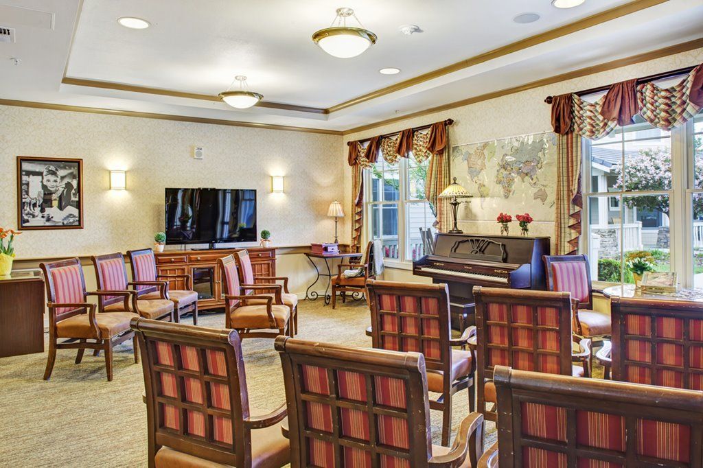 A well-arranged community room with chairs, a piano, and a television.
