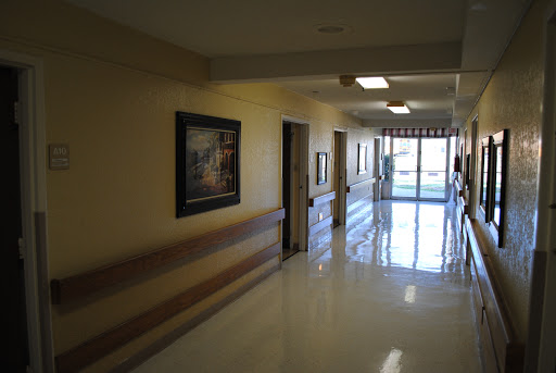 A well-lit hospital hallway featuring doors to patient rooms and framed artwork on the walls.