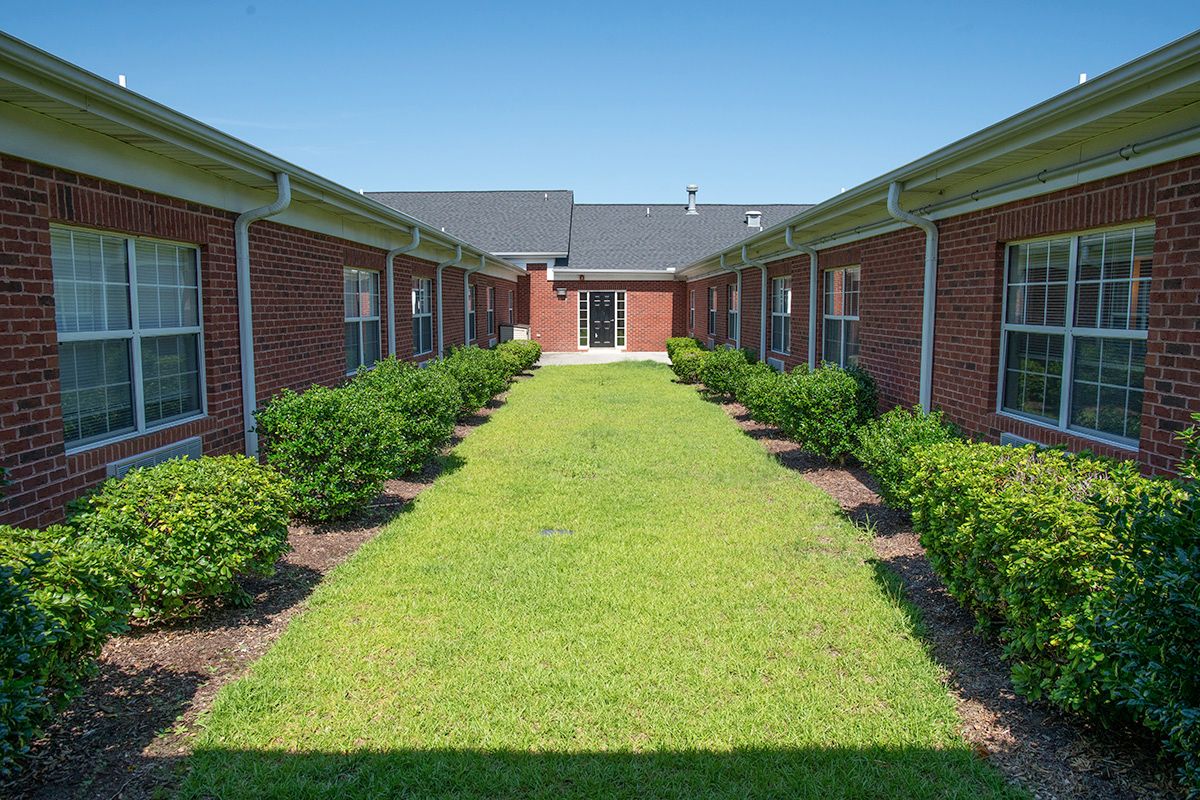 A neatly landscaped courtyard between brick buildings, featuring a grassy area flanked by bushes.