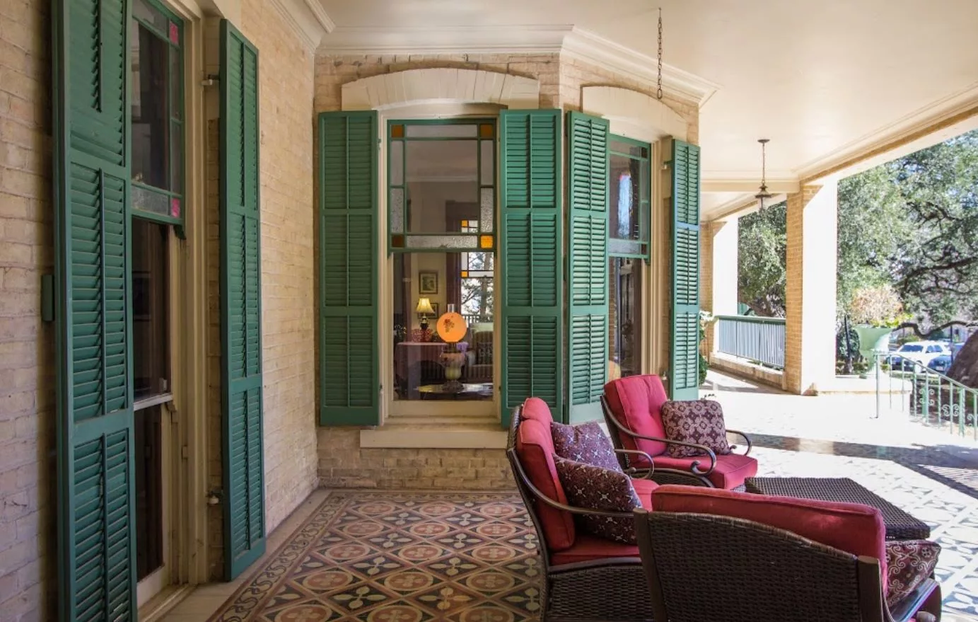 A cozy patio area with red-cushioned seating, green shutters, and vintage tiles.