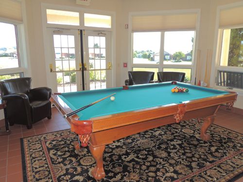 A well-lit game room with a pool table and comfortable chairs by the windows.