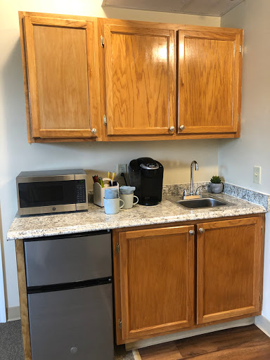 A compact kitchen setup featuring wooden cabinets, a microwave, coffee maker, and a small refrigerator.