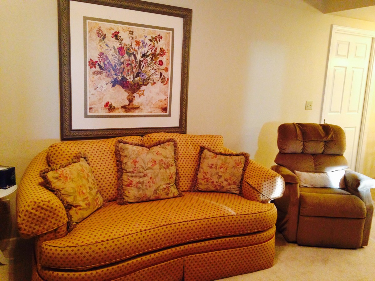 A cozy living room with a patterned sofa, recliner, and floral artwork hanging on the wall.