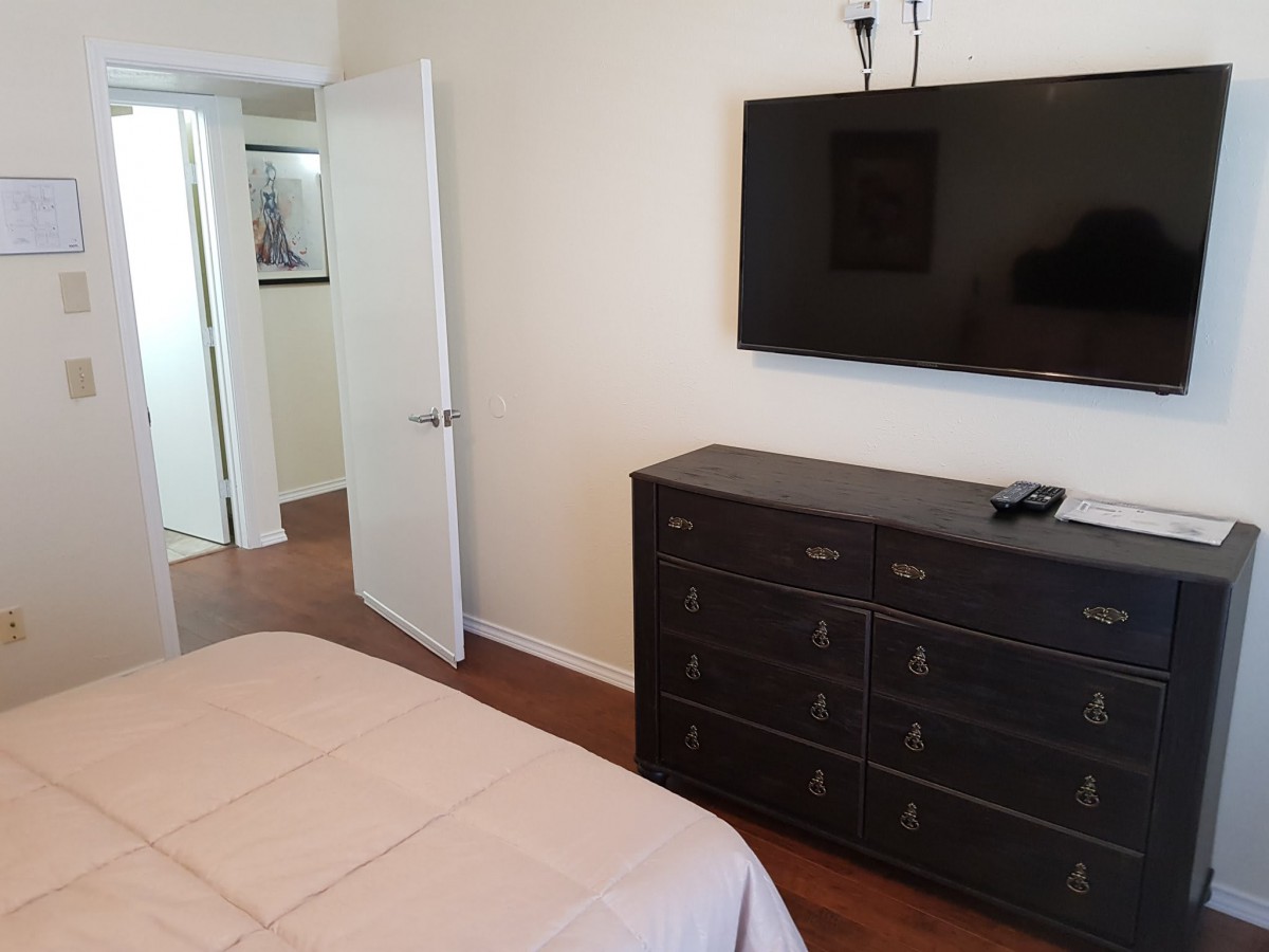 A minimalist bedroom with a mounted TV and dark dresser.