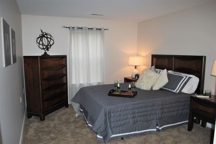 A cozy bedroom interior with a neatly made bed, decorative pillows, and a bedside lamp.