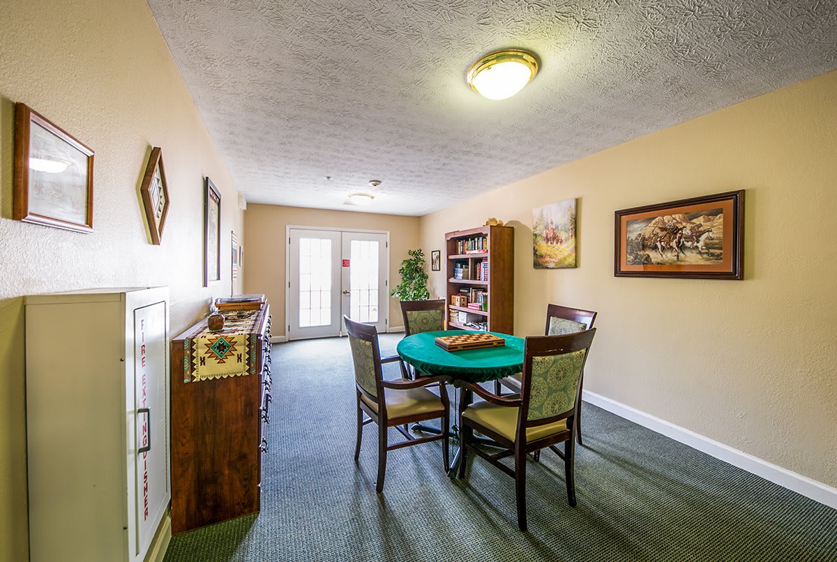 A cozy dining area with a table, chairs, and a bookshelf, illuminated by ceiling lights.