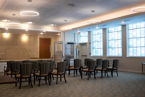 A spacious interior room featuring arranged chairs, modern lighting, and large windows.
