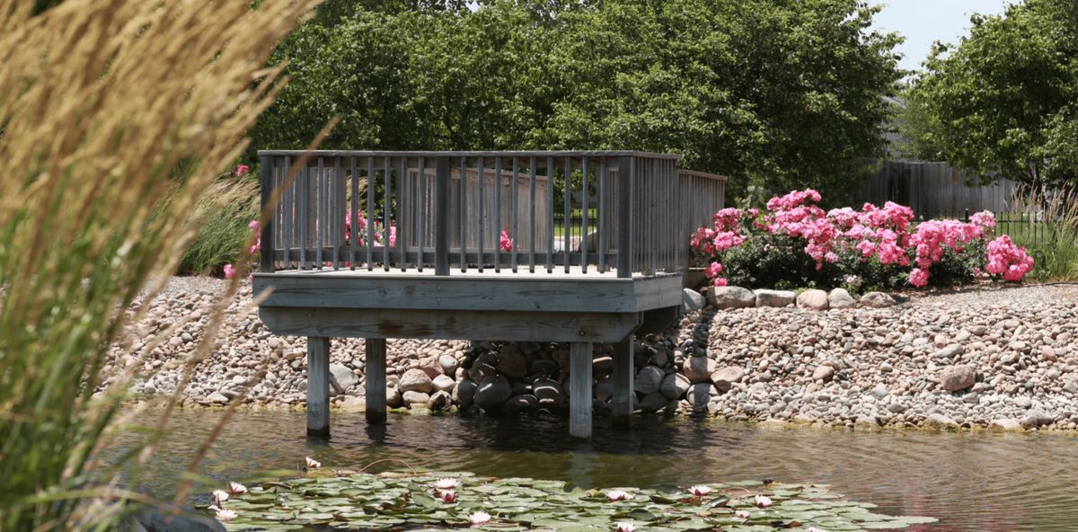 A tranquil garden scene with a footbridge over a pond adorned with lilies and surrounded by flowers.