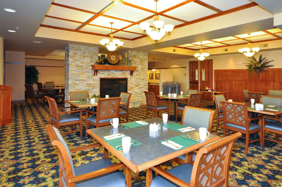 A cozy dining area with tables and chairs, featuring a fireplace and elegant chandeliers.