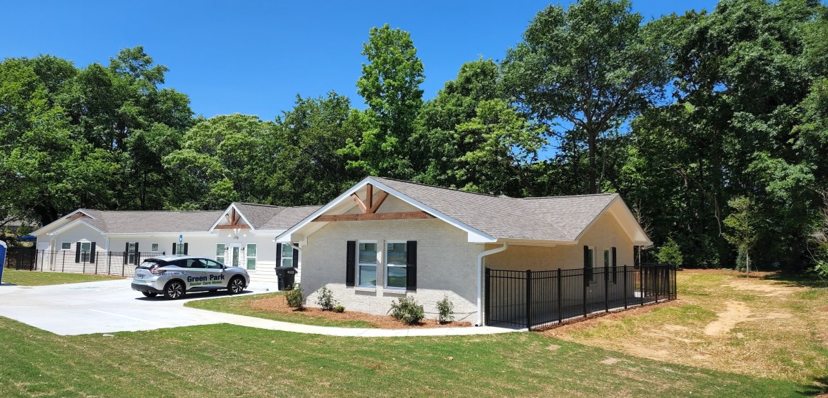 A suburban residential house with a well-maintained yard and surrounding trees under a clear blue sky.