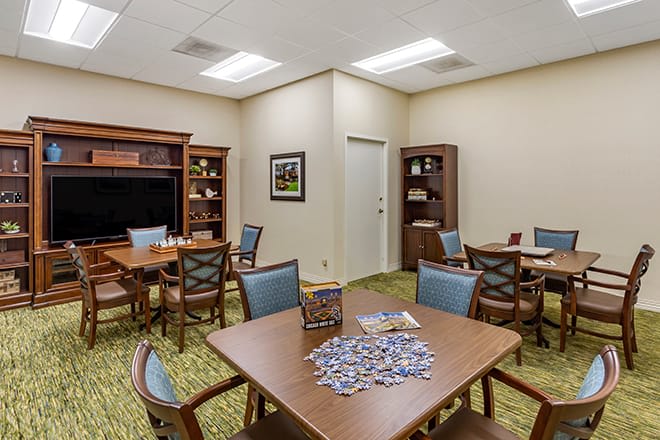 A well-lit room with multiple tables, puzzles, and bookshelves.
