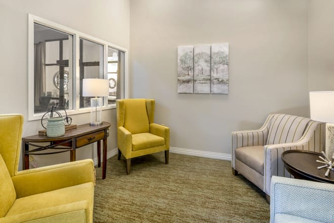 A cozy living room with two yellow armchairs and a striped chair, complemented by a lamp and wall art.