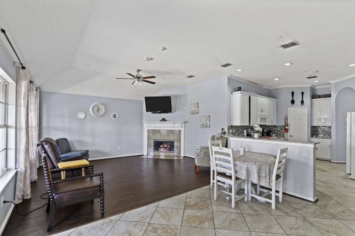 A modern open-floor plan living area featuring a living room with a fireplace, a small dining table, and a kitchen.
