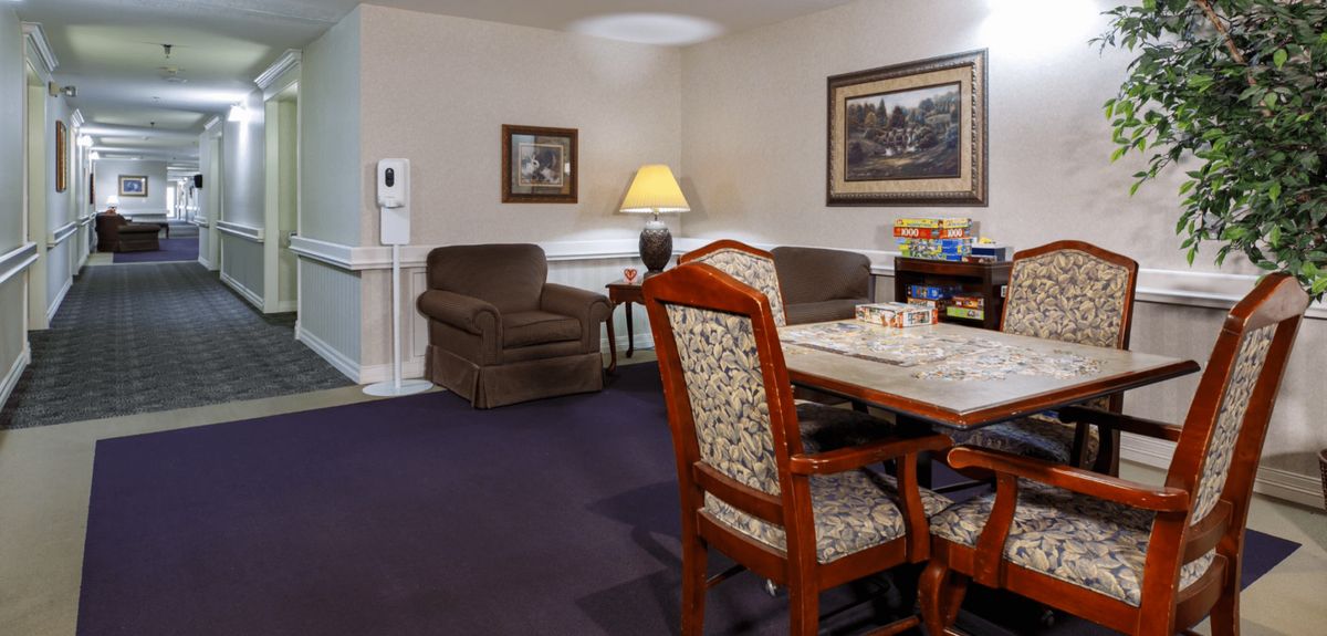 A cozy living room with a table and chairs, a lamp, and framed paintings on the walls.