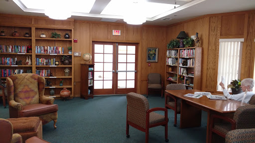 A cozy library space featuring wooden walls, bookshelves filled with books, and comfortable chairs.