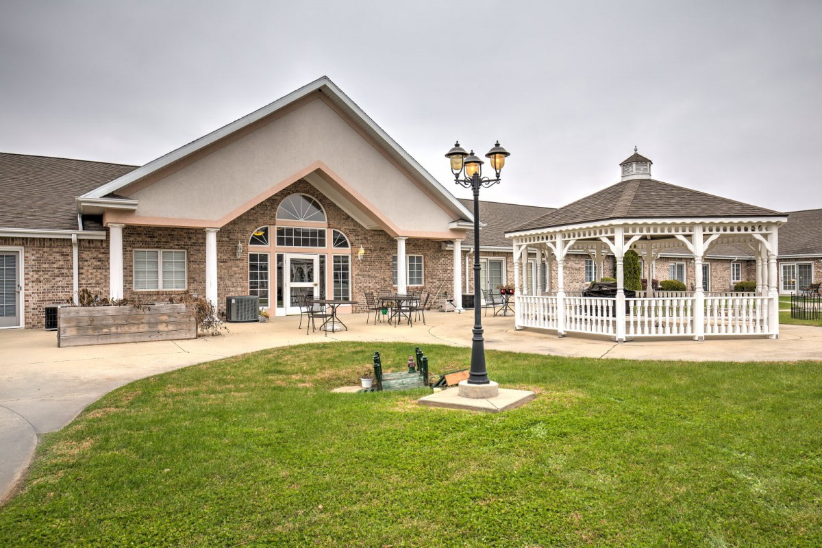 A view of a building with a gazebo and a lamp post on a well-maintained lawn.