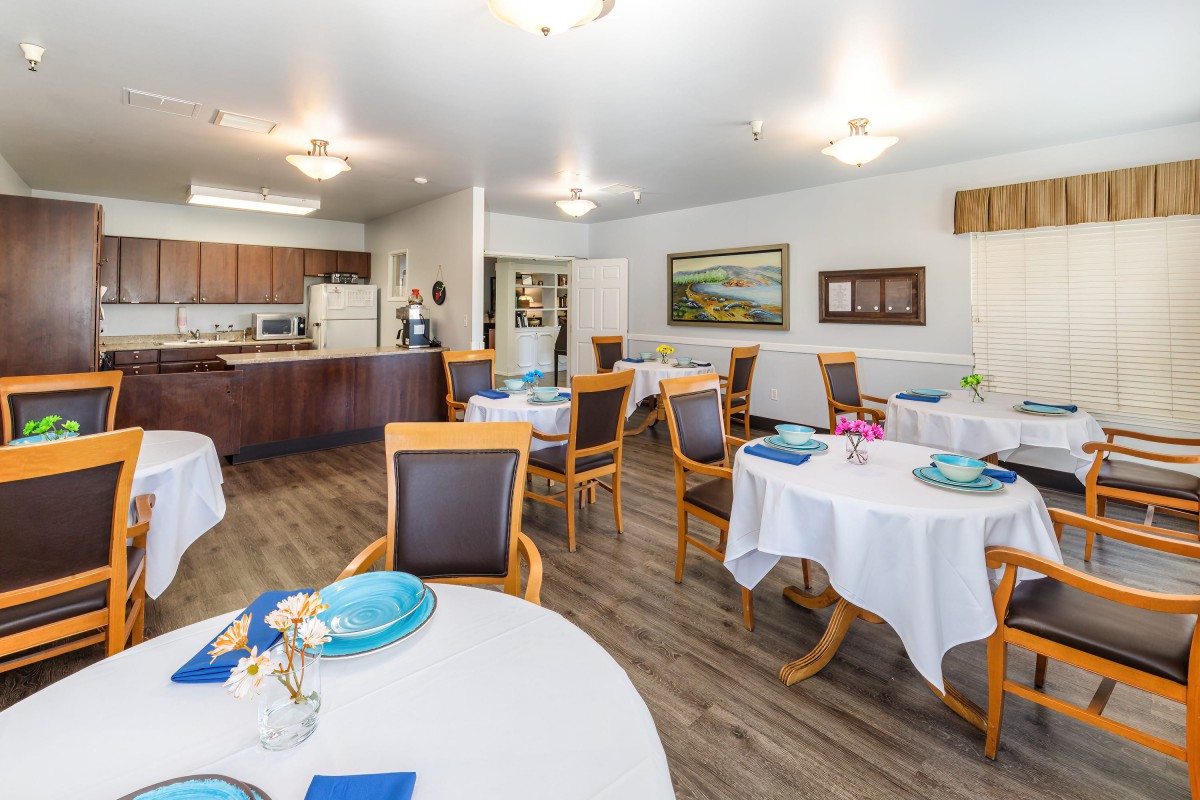 A well-lit dining area with set tables and chairs adjacent to a kitchen.