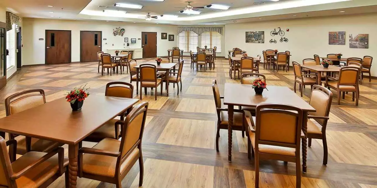 A spacious dining room with wooden floors, featuring neatly arranged tables and chairs.