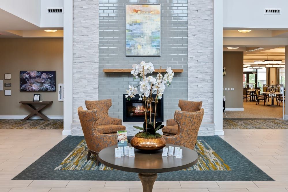 A modern lobby features a cozy seating area with four chairs around a table adorned with orchids, set against a backdrop of a fireplace and artwork.