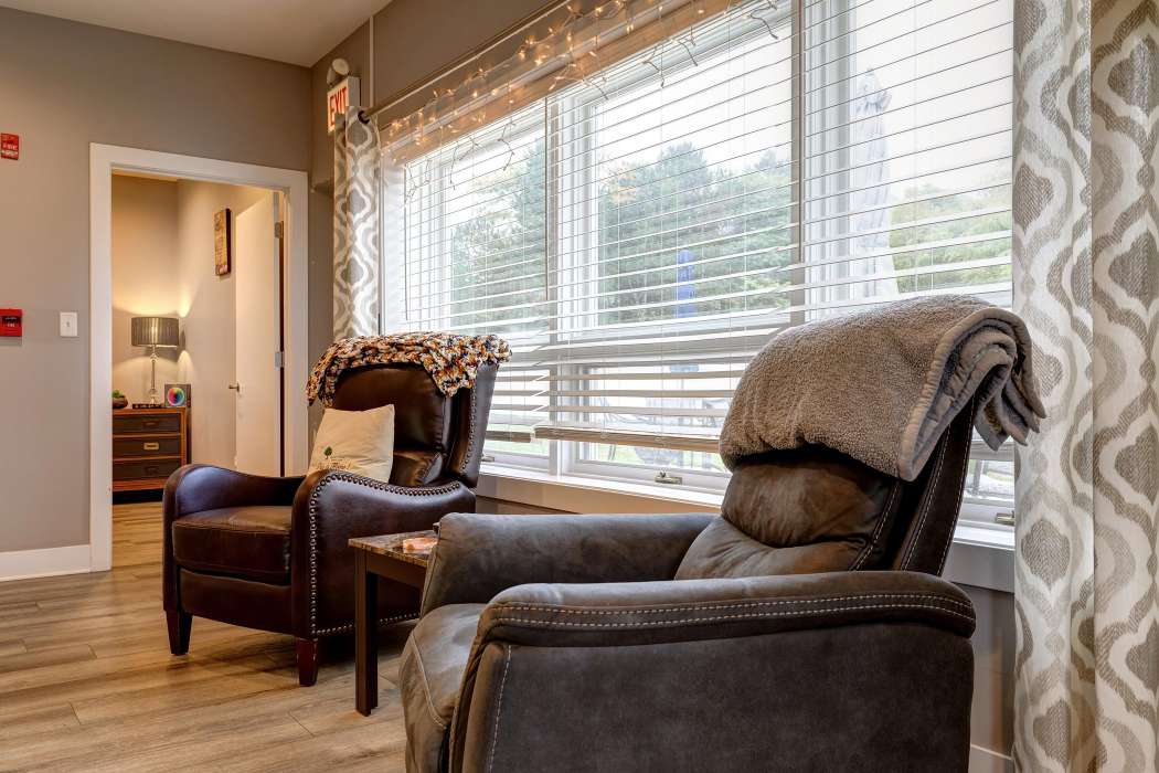 A cozy living room with comfortable chairs and large windows with blinds.