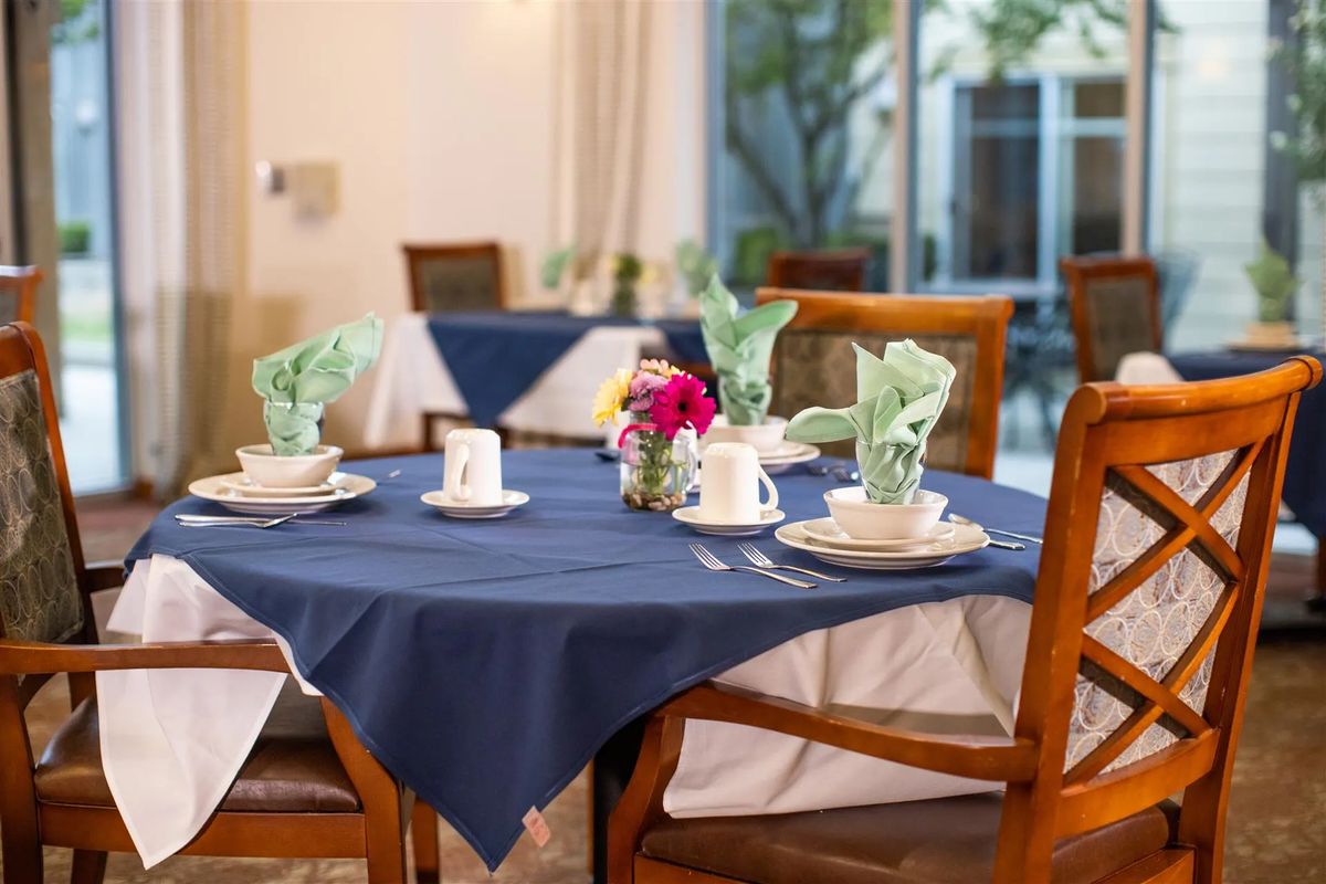 A neatly set dining table with blue tablecloths, cups, and floral centerpiece in a restaurant setting.