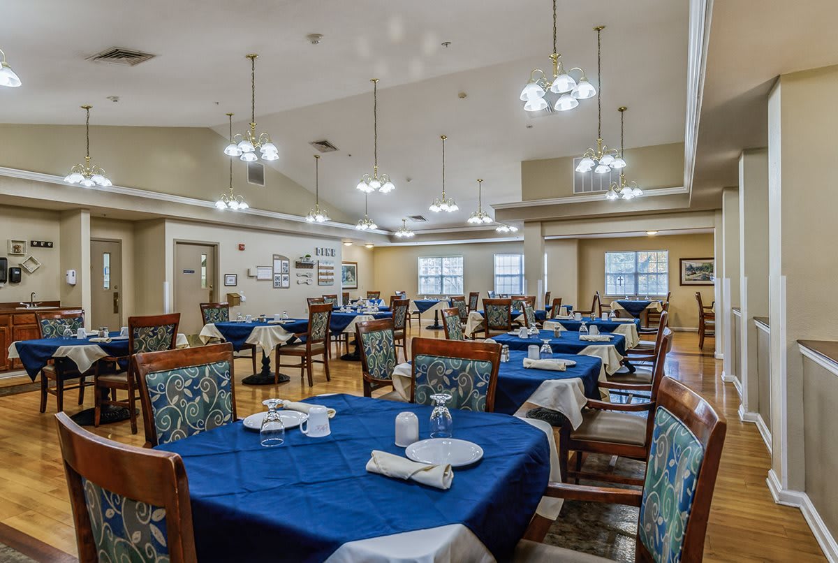 A spacious dining room with neatly set tables featuring blue tablecloths and elegant lighting.