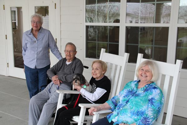 A group of seniors sitting on a porch in rocking chairs, enjoying the day.