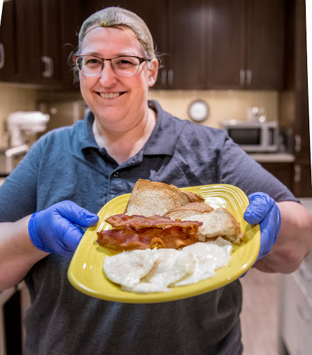 A cheerful person proudly displaying a delicious meal in a kitchen setting.