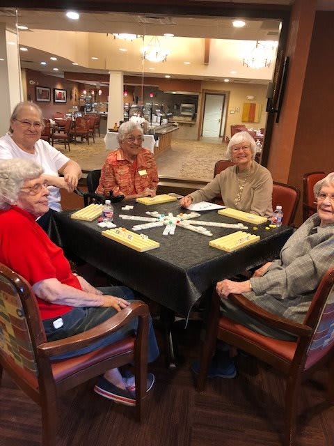 A group of seniors seated around a dining table in a communal setting.