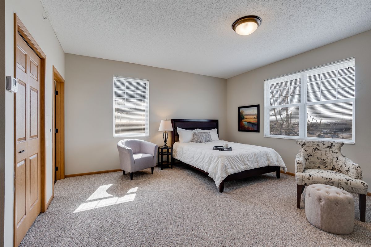 A cozy bedroom with a neatly made bed, armchairs, and warm lighting.